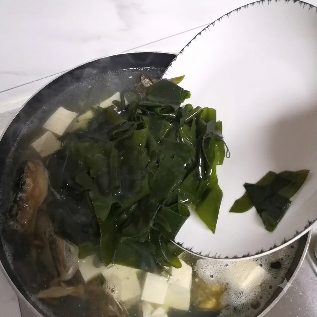 Trozos de alga deslizándose desde un plato hacia la olla de sopa a fuego lento.