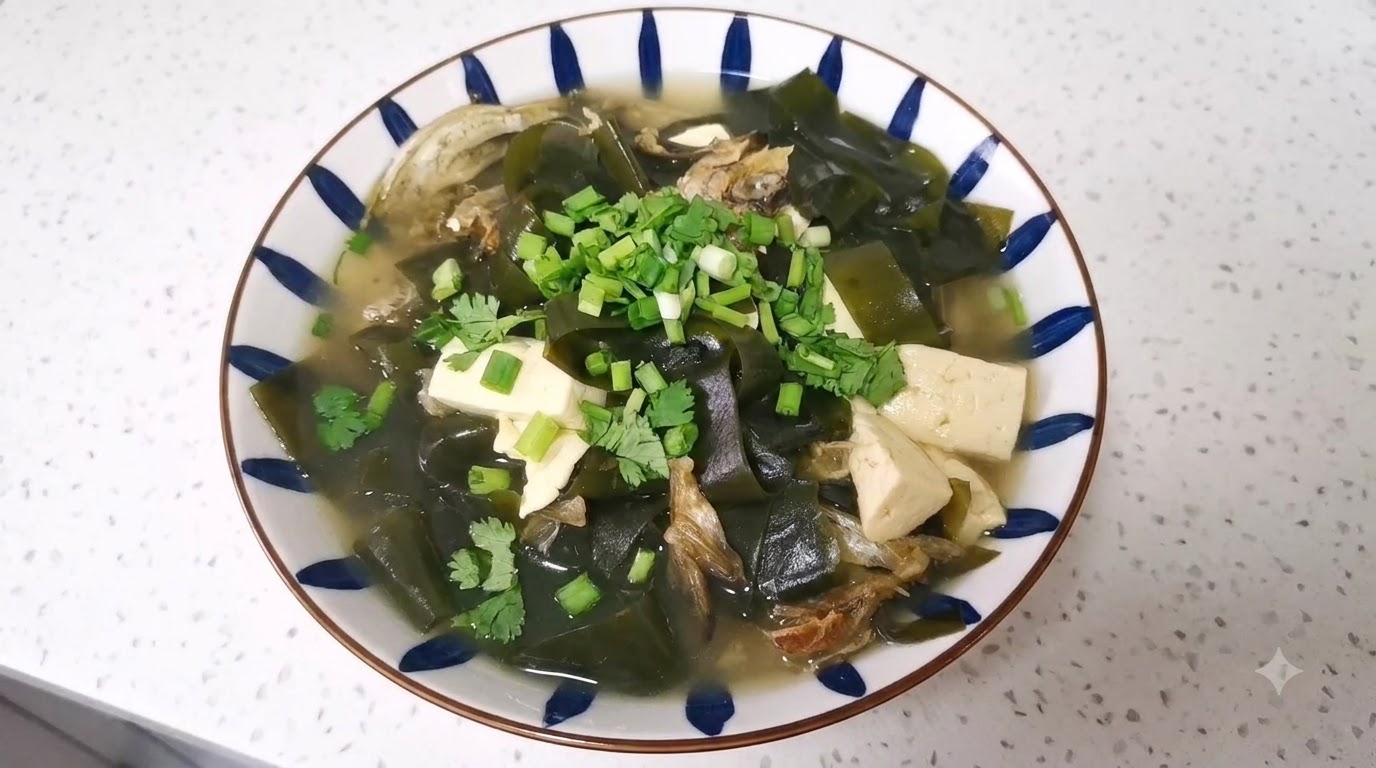 Un plato de sopa de cabezas de abadejo y tofu con algas, decorado con cebollino y cilantro en un cuenco blanco con patrones azules.