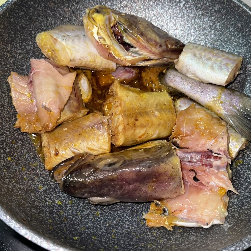 Trozos de abadejo sellándose en la sartén junto con patatas amarillas en rodajas.