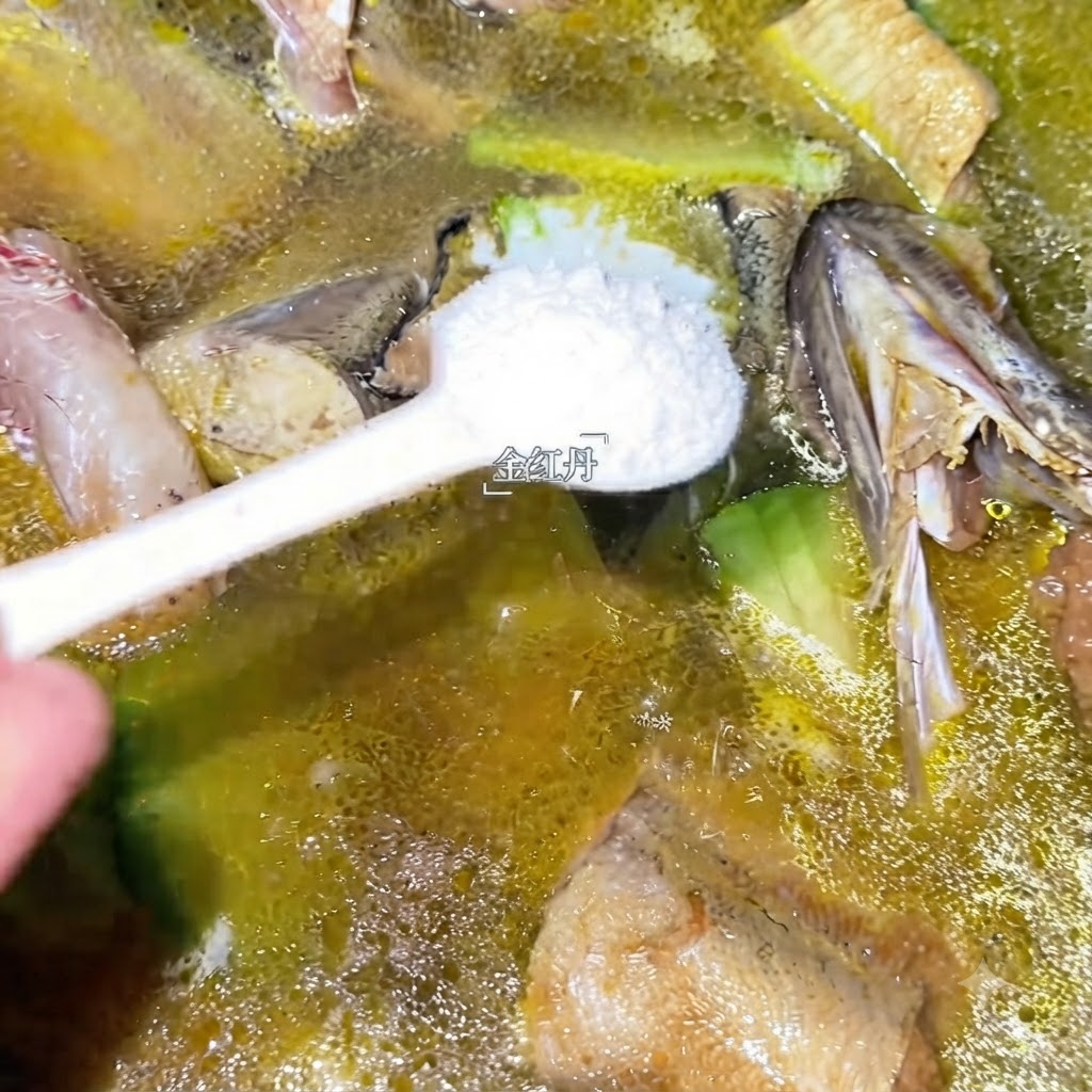 Una cucharada de condimento blanco siendo añadida a la olla de sopa de abadejo a fuego lento.