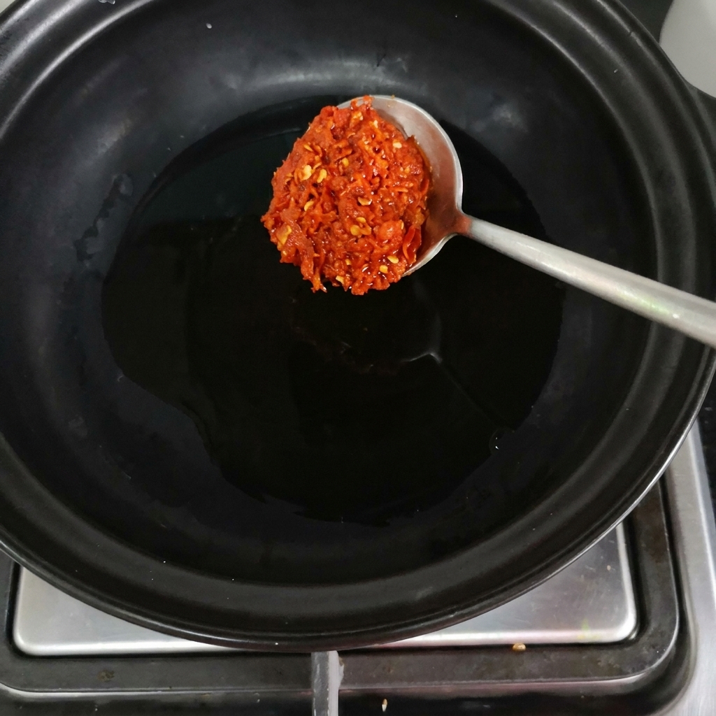 Una cucharada de pasta de chile rojo cayendo en una olla de barro negro sobre el fuegocite: 1.