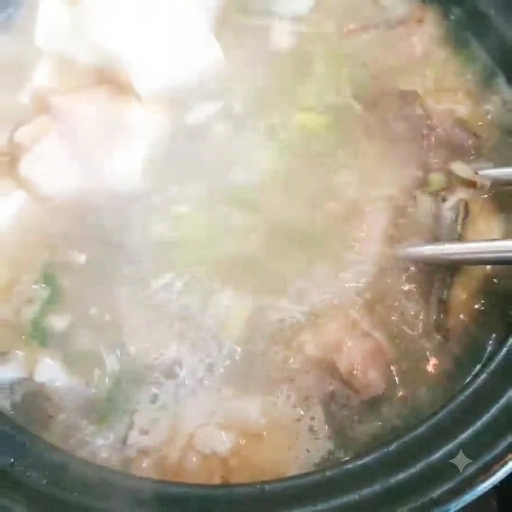 Cubos de tofu siendo añadidos a una olla de sopa de pescado burbujeante con cebollas verdes.