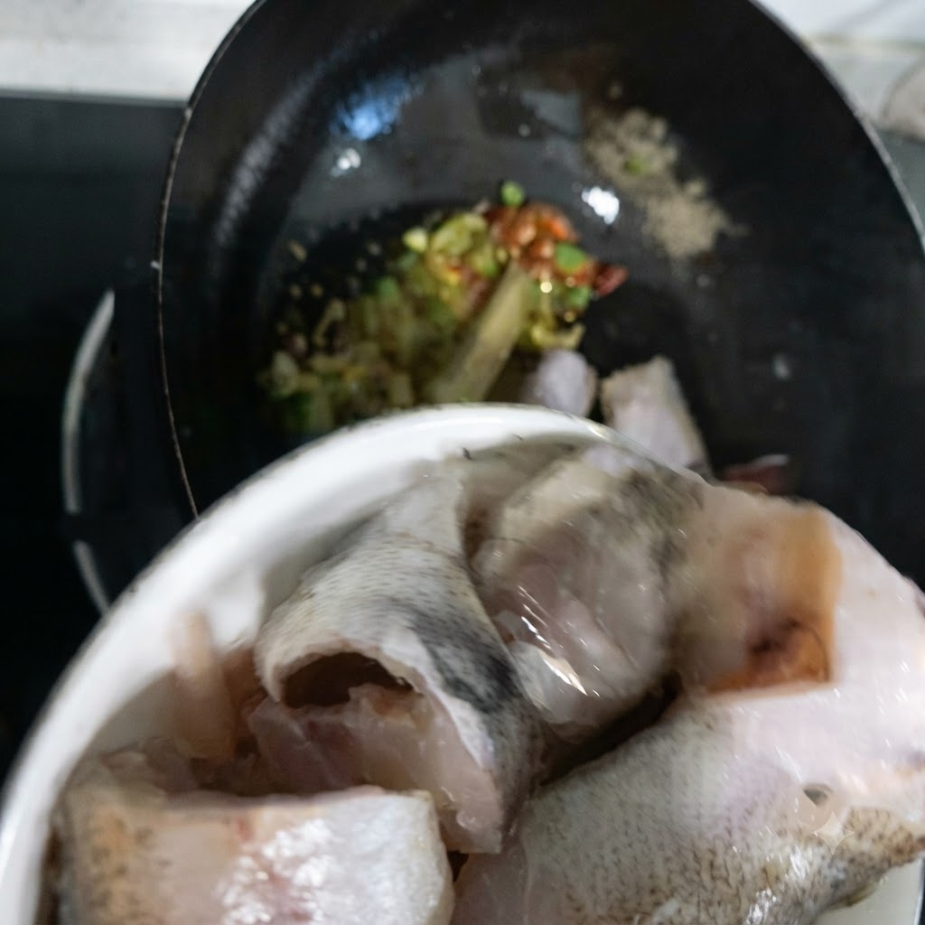 Trozos de pescado abadejo siendo transferidos desde un tazón hacia el wok.
