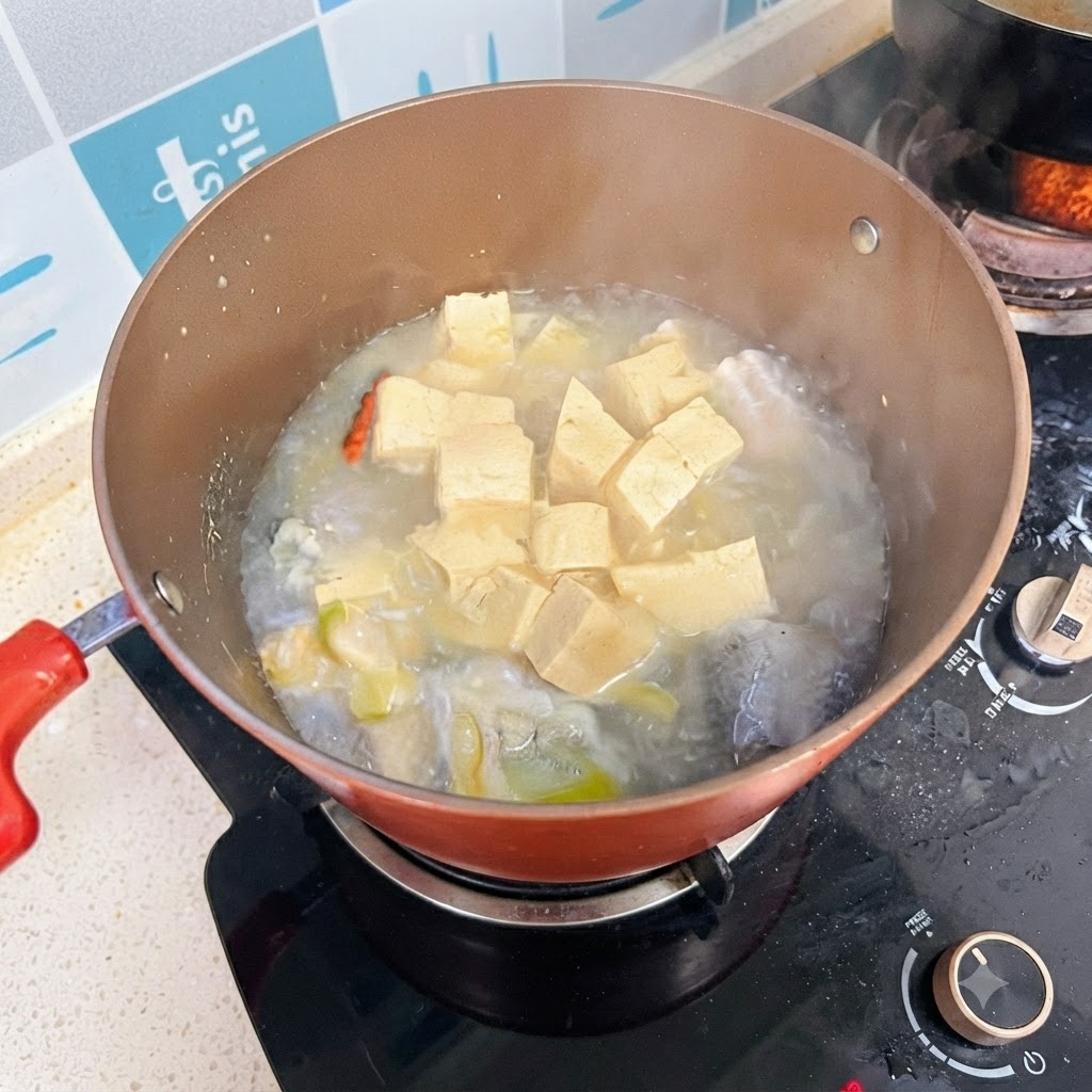 Una olla de sopa de pescado y tofu cocinándose a fuego lento con un caldo blanco lechoso.