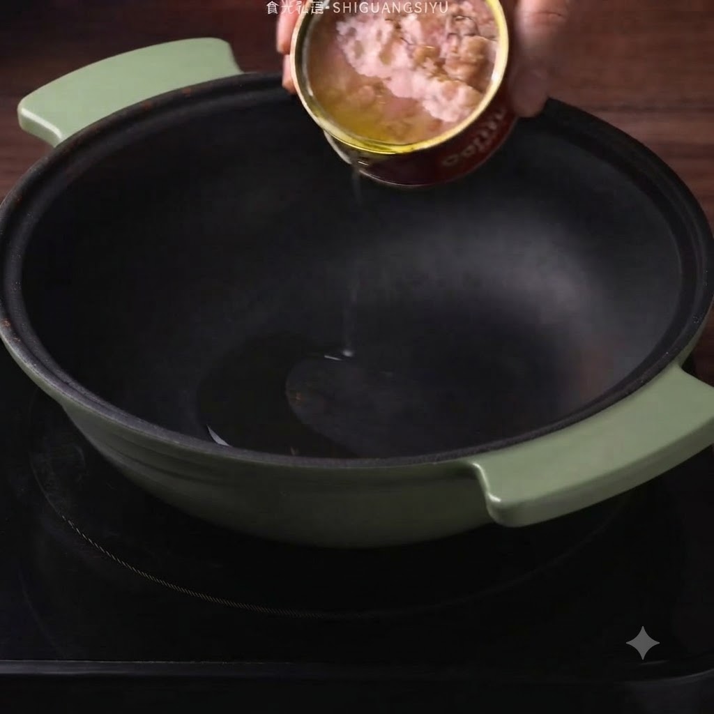 Aceite de atún en lata siendo vertido desde una lata en una olla verde oscura.
