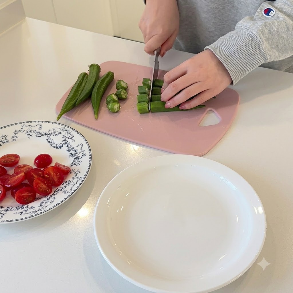 Manos cortando okra verde en rodajas pequeñas y circulares sobre una tabla de cortar rosa.