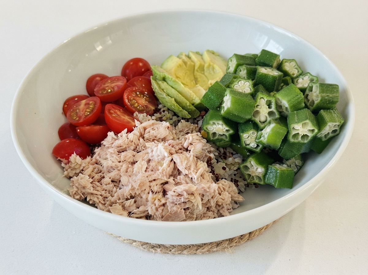 Un bol blanco relleno con una base de arroz, cubierto con secciones de atún, tomates cherry, aguacate en rodajas y okra.