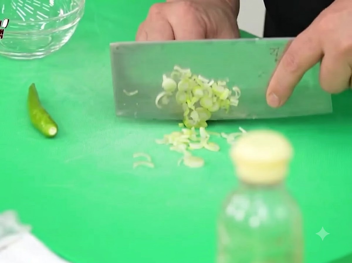 Cebollines, chiles Cheongyang y cebollas picándose finamente sobre una tabla de cortar verde con un cuchillo de chef.