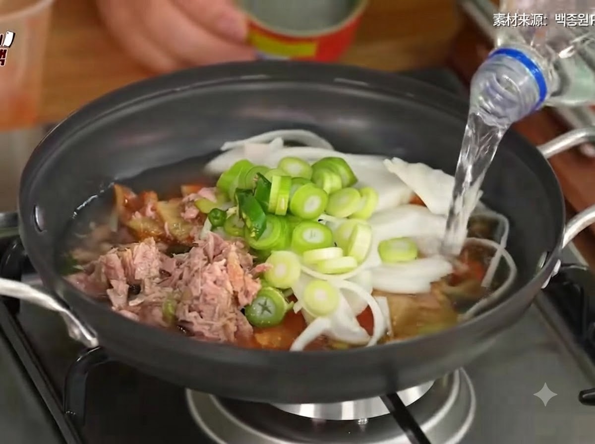 Agua siendo vertida en la olla que contiene el kimchi, las verduras y el atún.