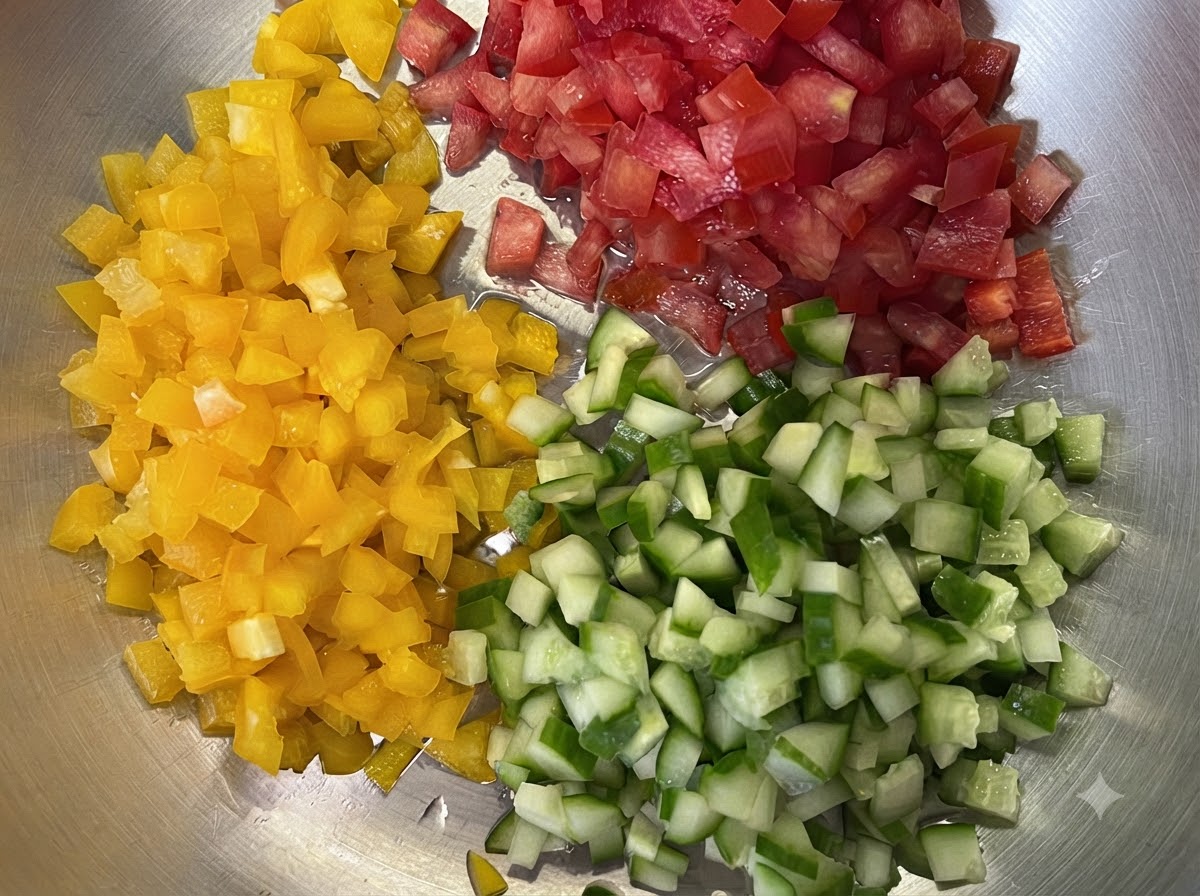 Pimientos amarillos, tomates rojos y pepinos verdes cortados finamente en cubos pequeños sobre una bandeja.