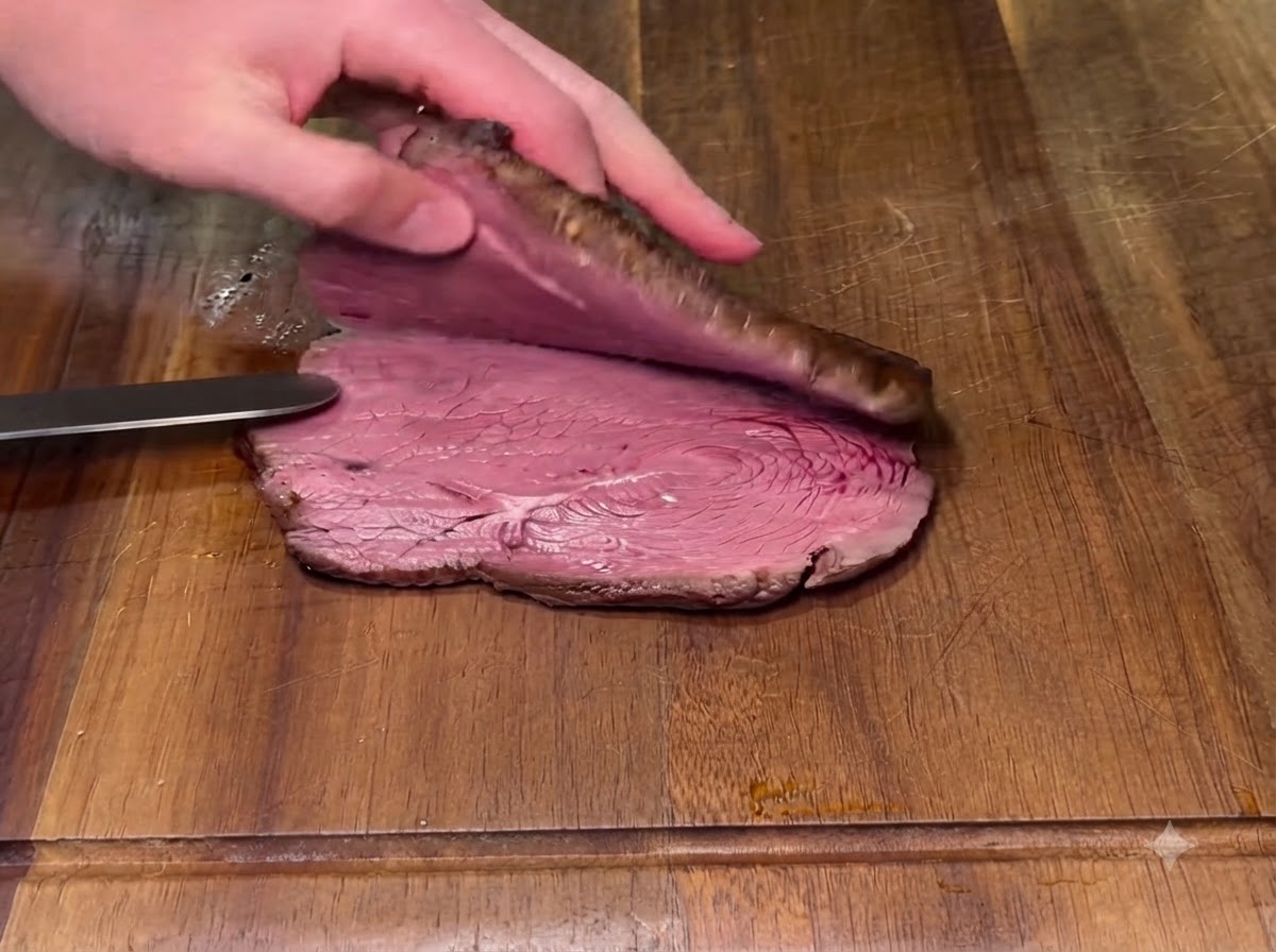 Un filete cocinado siendo cortado horizontalmente por la mitad en una tabla de cortar de madera con un cuchillo.