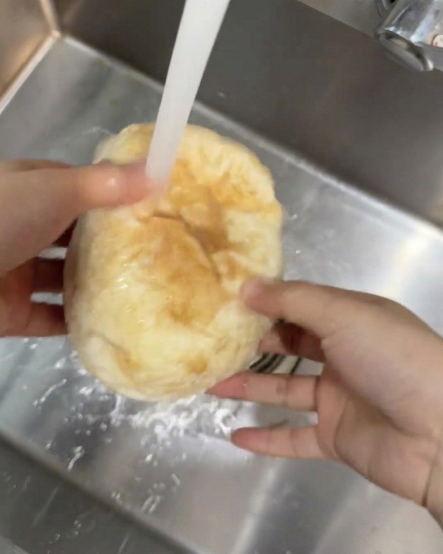 Un pan ciabatta redondo siendo sostenido bajo una corriente de agua corriente del grifo en el fregadero de la cocina.