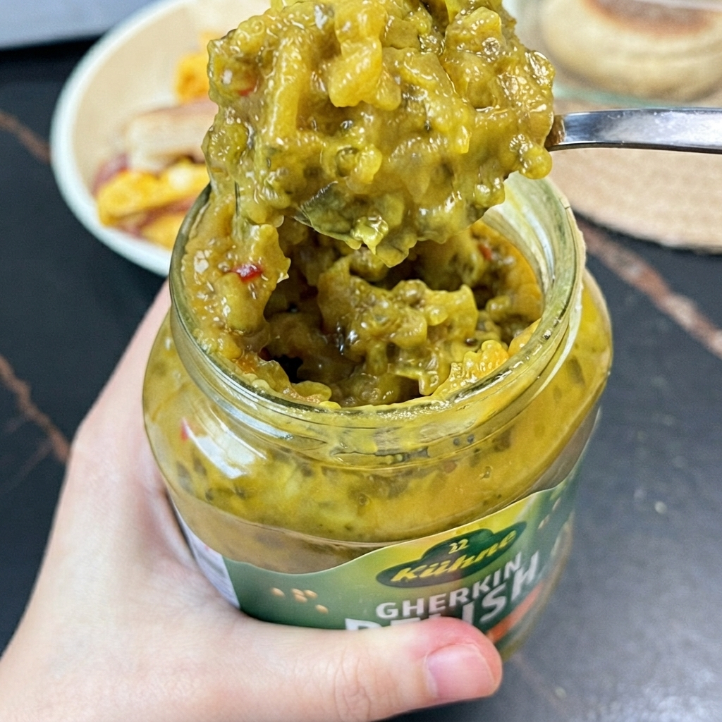 Una cucharada de salsa verde brillante de pepinillos extraída de un frasco de vidrio con una cuchara pequeña.