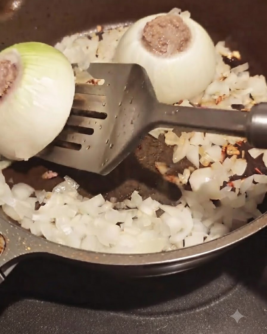 Una espátula volteando un aro de cebolla relleno de carne en una sartén con trozos de cebolla picada alrededor.
