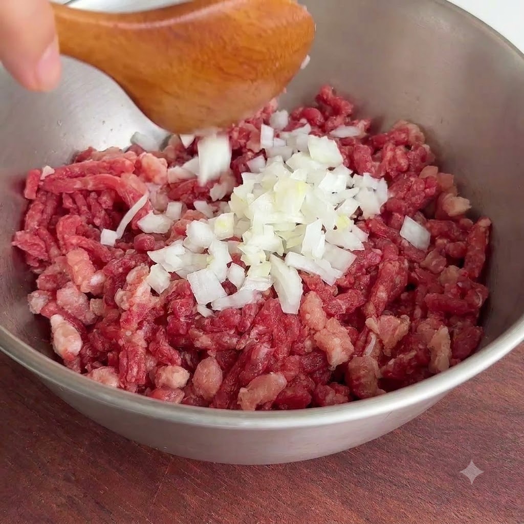 Un montón de trozos de cebolla blanca recién picados cayendo desde una cuchara de madera a un tazón de metal con carne picada cruda.