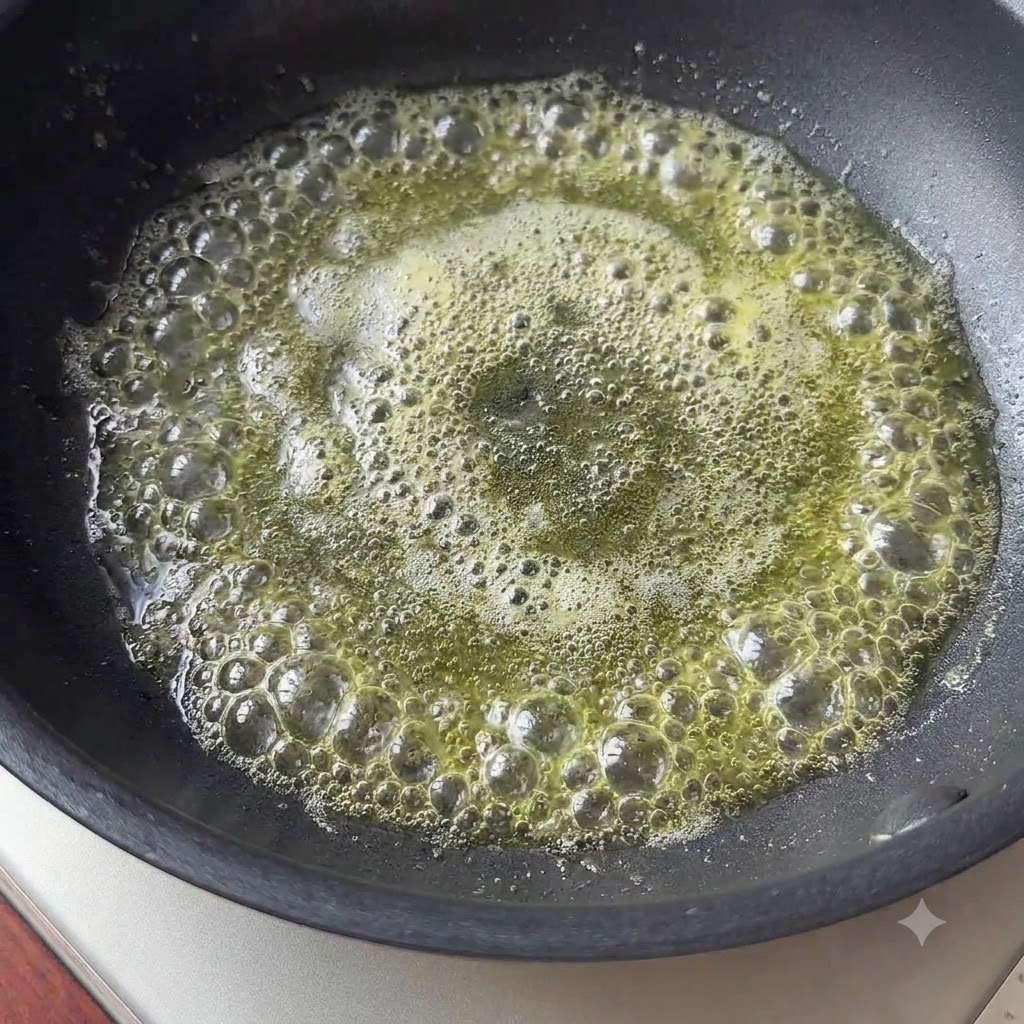 Un trozo pequeño de mantequilla derritiéndose y burbujeando en una sartén negra.