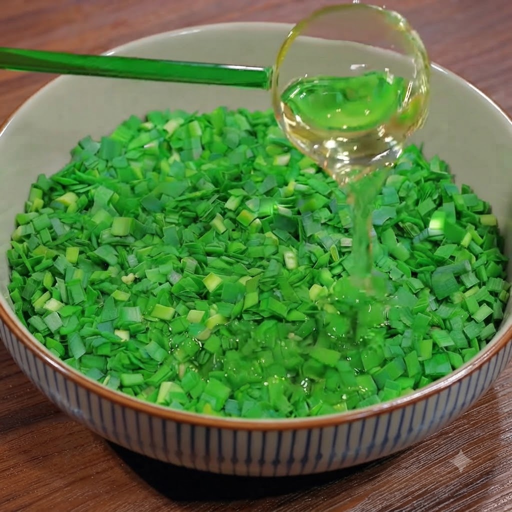 Un cucharón vertiendo aceite de cocina sobre un bol lleno de cebollino verde recién picado.