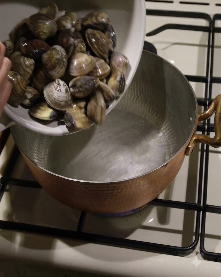 Almejas frescas pasadas de un bol blanco a una olla de cobre martillado sobre el fuego.