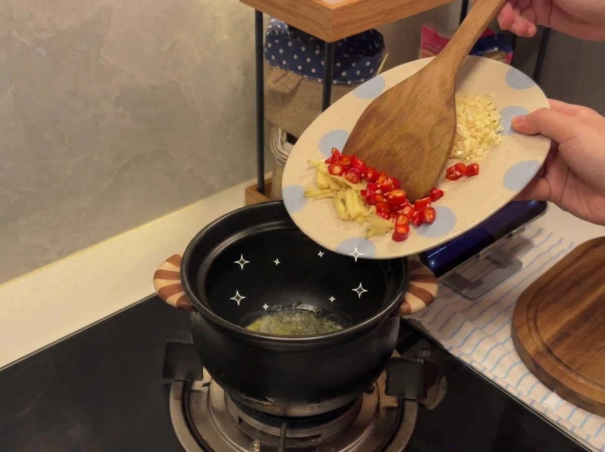 Ajo picado y chiles siendo transferidos desde un plato con motivos hacia una olla de cerámica que contiene mantequilla derretida.