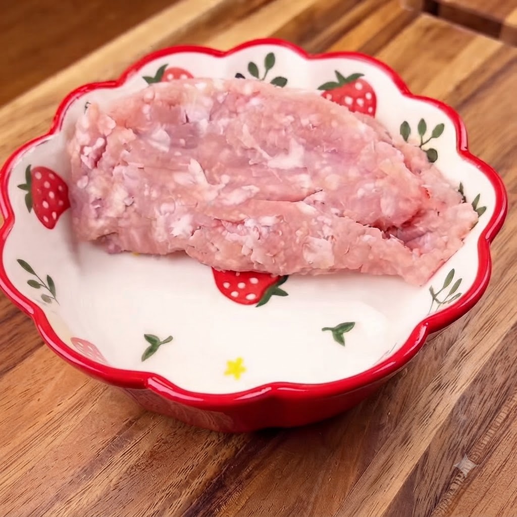 Carne de cerdo picada dentro de un tazón con motivos florales, cubierta con cebollín fresco picado.