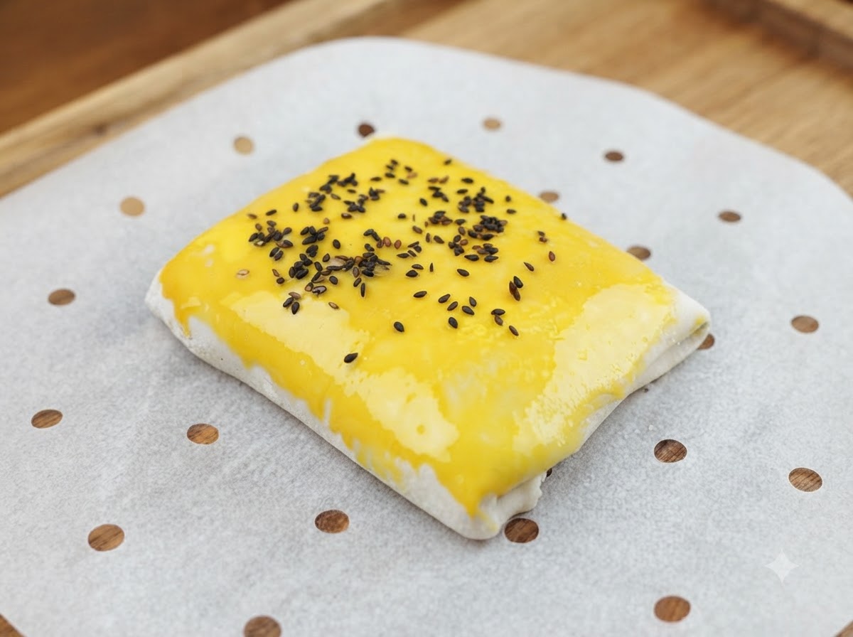 Semillas de sésamo negro siendo espolvoreadas sobre la superficie barnizada con huevo del pastelito de carne.