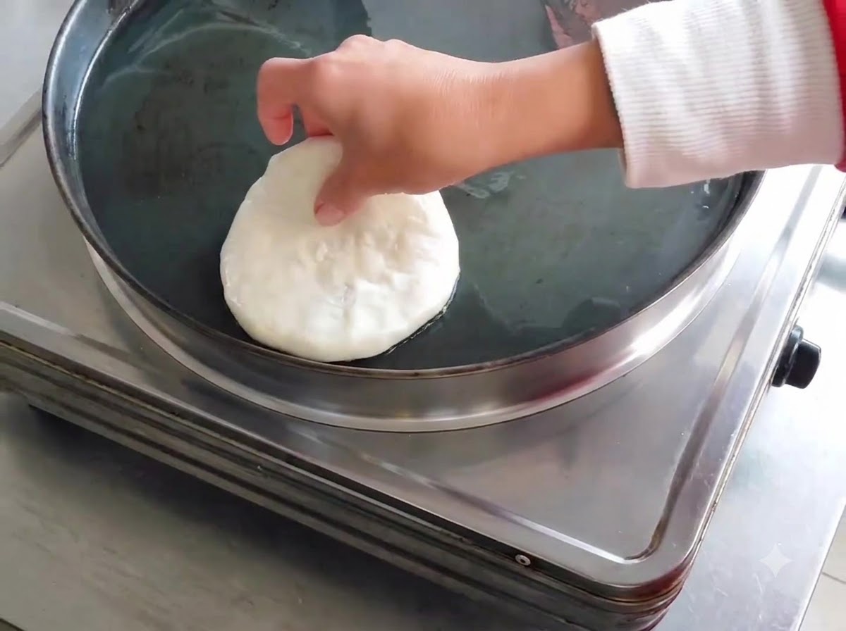 Una empanada de carne cruda colocándose en una sartén eléctrica aceitada.