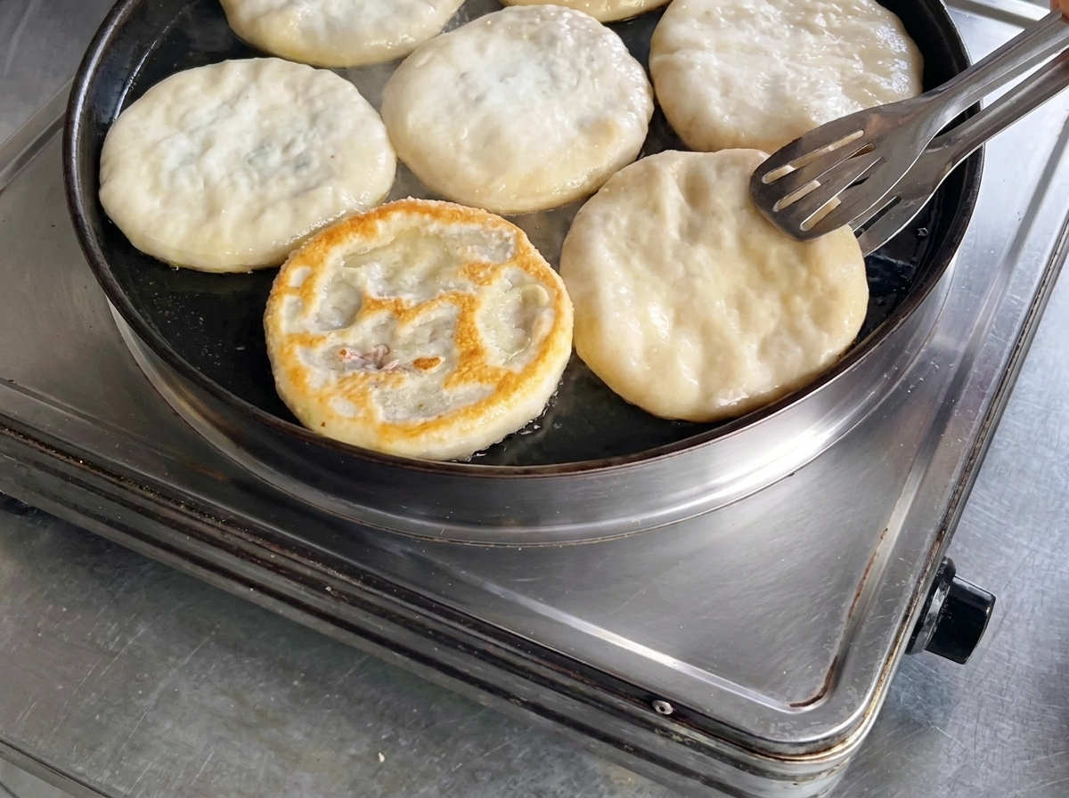 Usando unas pinzas de metal para dar la vuelta a una empanada de carne en la sartén, revelando una superficie perfectamente dorada y crujiente.