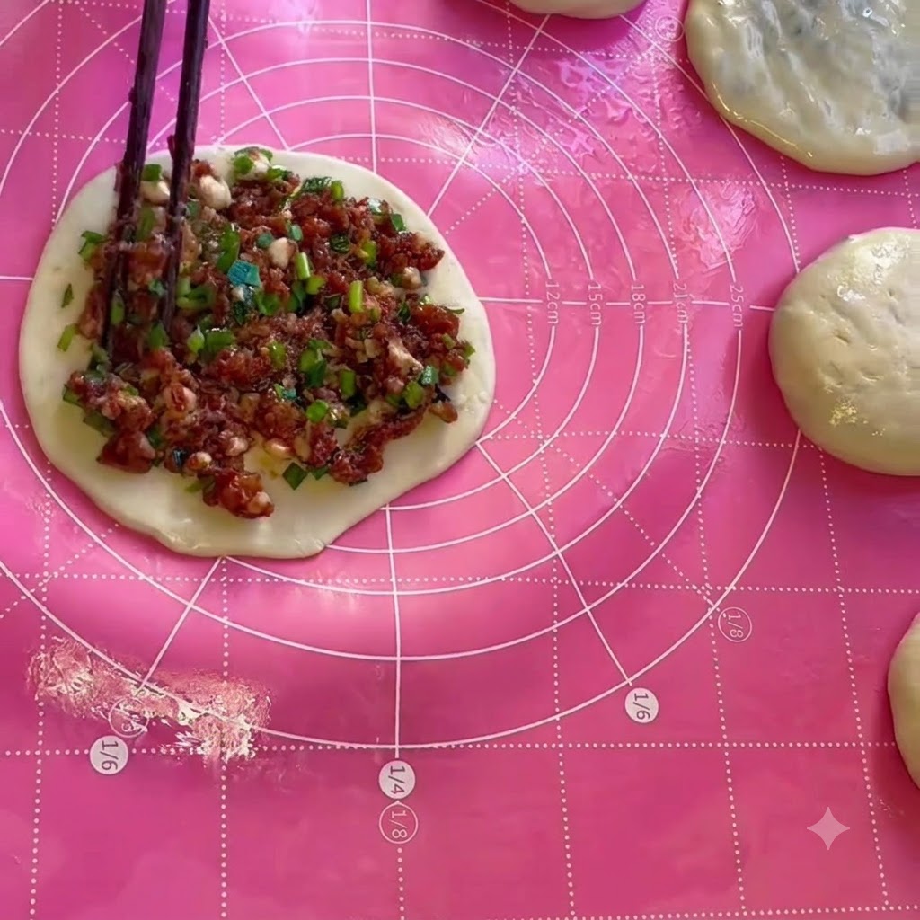 Relleno de carne y cebollino siendo extendido uniformemente sobre una hoja circular de masa usando palillos.