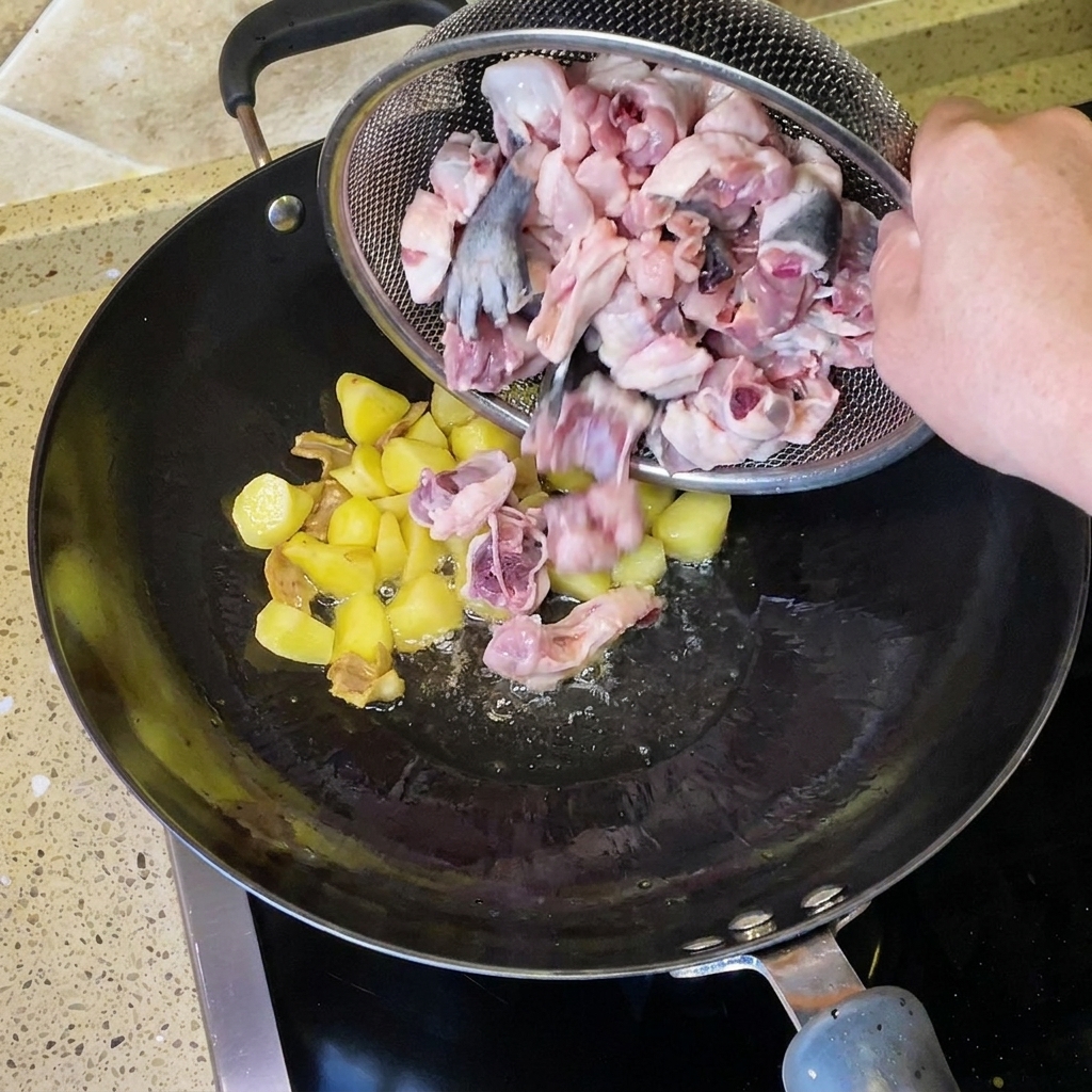 Trozos de pollo crudo picado siendo vertidos desde un colador de alambre hacia el wok con patatas fritas y jengibre.