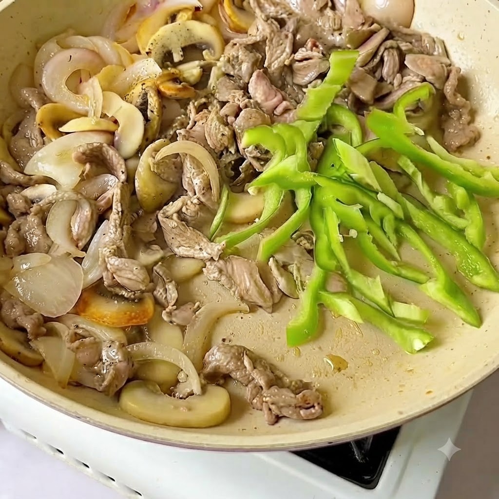 Rodajas de pimiento verde fresco añadidas a la sartén junto con la ternera y las cebollas.