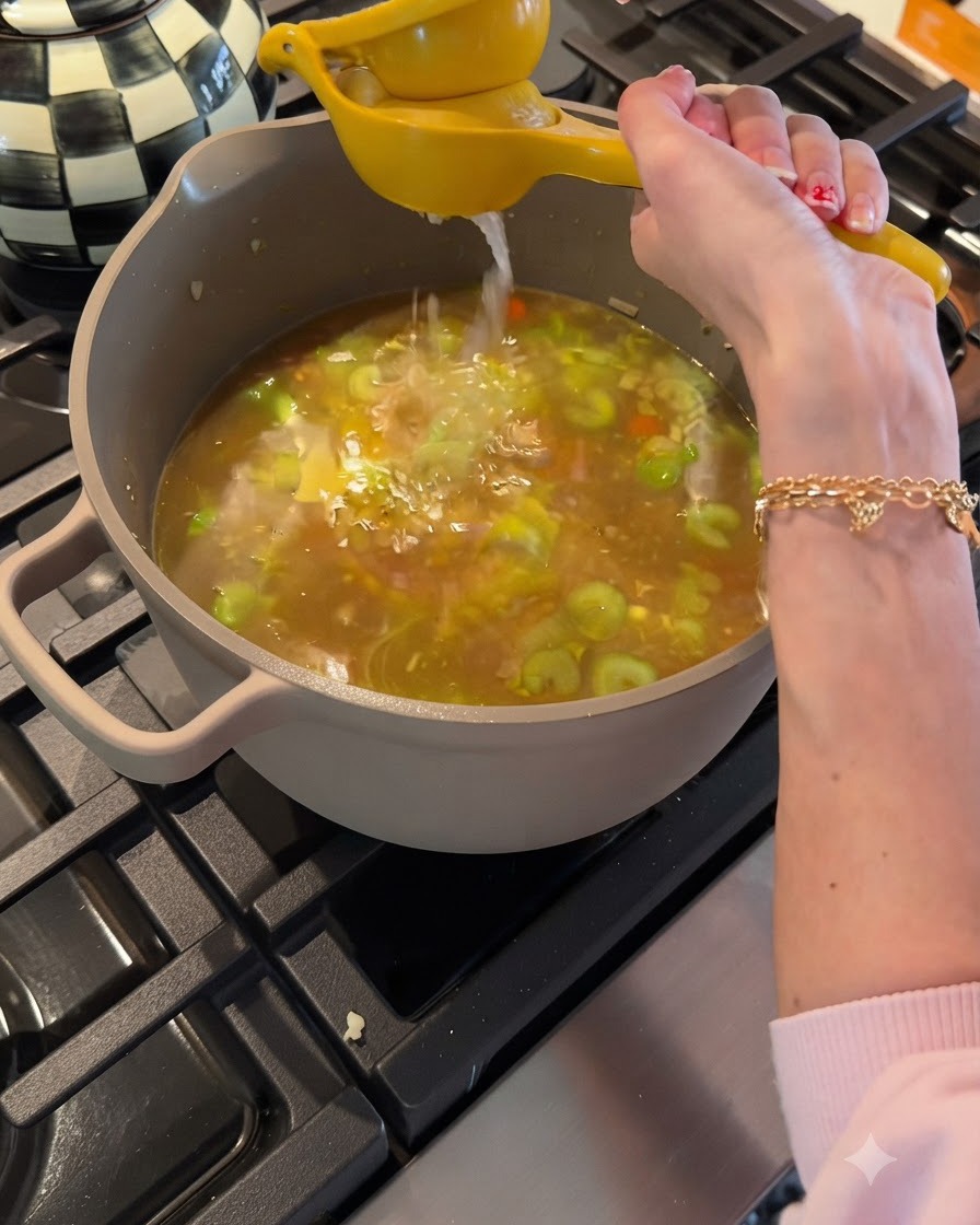 Exprimiendo jugo de limón fresco de un exprimidor amarillo hacia una olla con caldo y verduras a fuego lento.