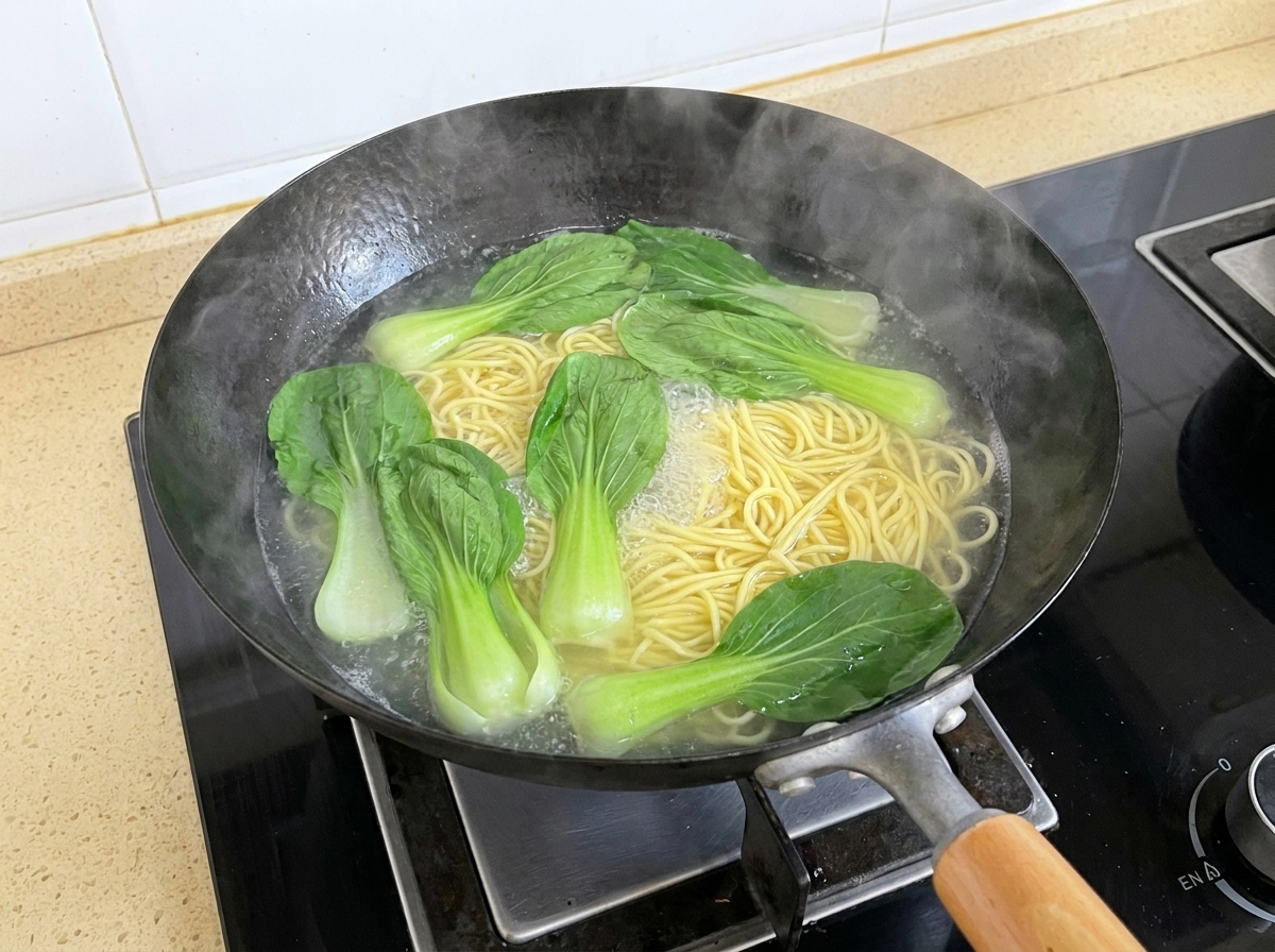 Hojas de bok choy fresco flotando en agua hirviendo junto con fideos en ebullición en un wok.