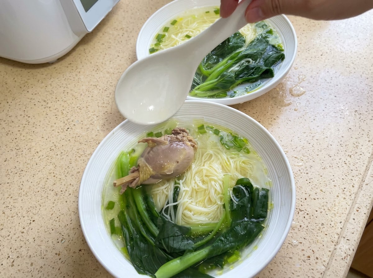 Un bol de fideos cubierto con un trozo de pollo y bok choy cocinado.