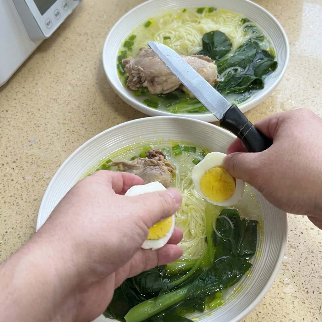 Manos cortando un huevo duro por la mitad con un cuchillo sobre un bol de fideos con sopa.