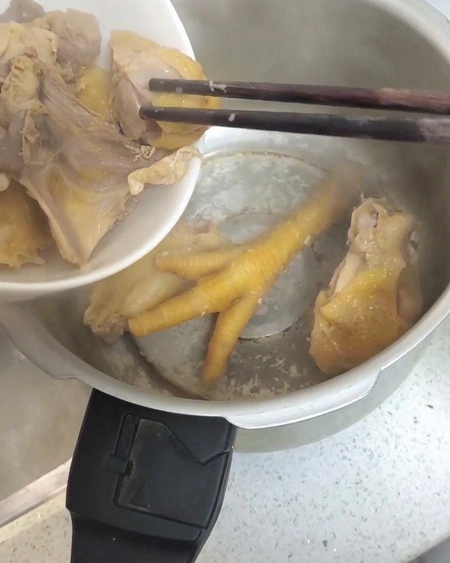 Piezas de pollo blanqueado siendo transferidas con palillos a una olla a presión de acero inoxidable.