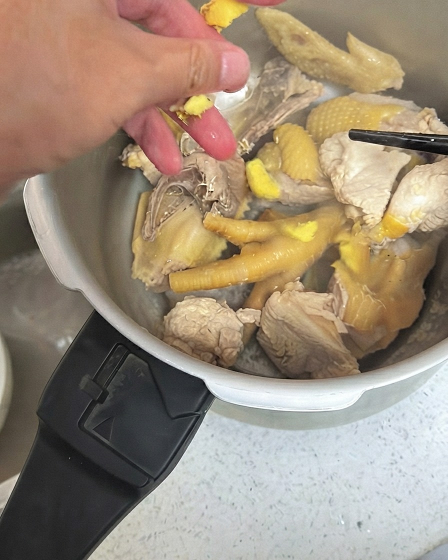 Trozos de jengibre machacado siendo esparcidos sobre el pollo dentro de una olla a presión.