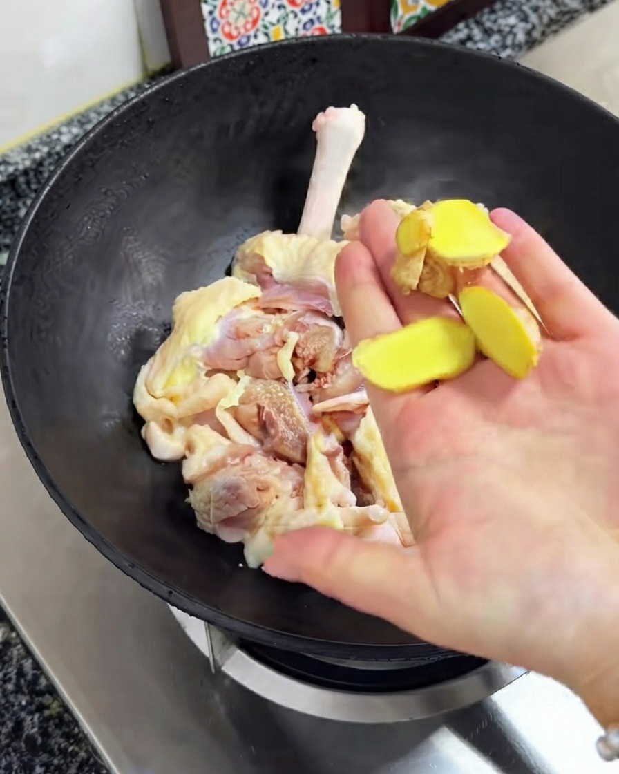 Rodajas de jengibre fresco sobre el pollo crudo dentro del wok negro.