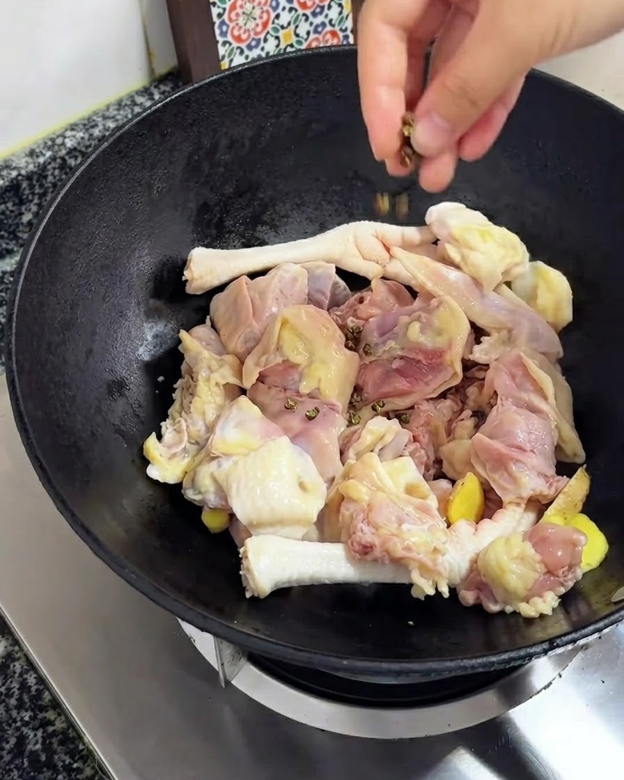 Pimienta de Sichuan cayendo sobre el pollo y el jengibre en el wok.