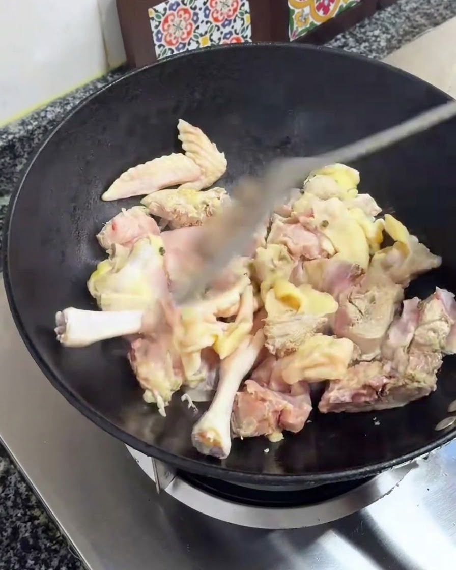 Trozos de pollo siendo salteados con una espátula en un wok negro sobre el fuego.