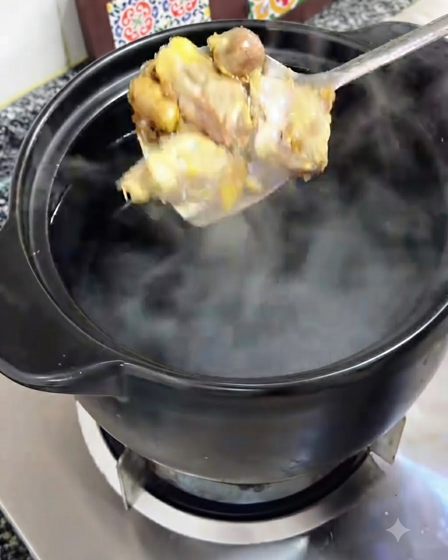 Trozos de pollo dorado siendo pasados con una cuchara a una olla de barro negra con agua hirviendo.