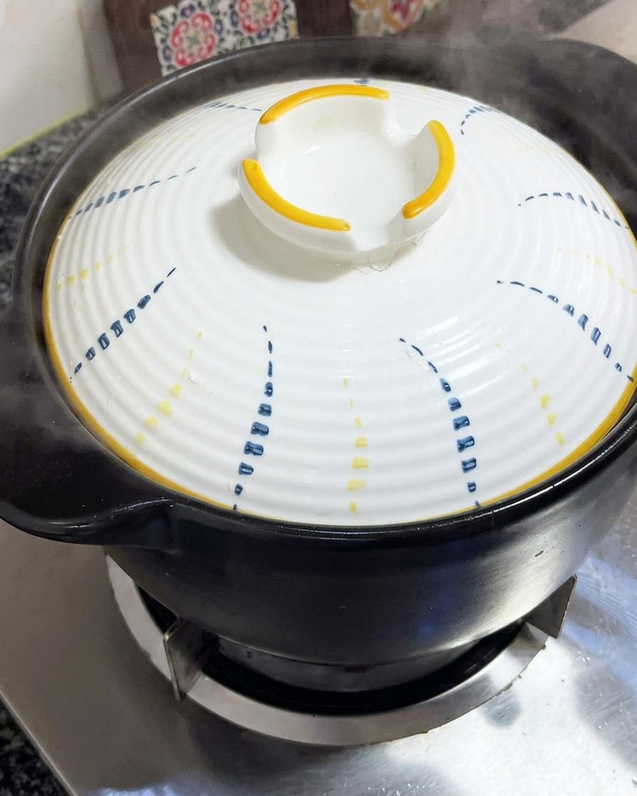 Una tapa blanca con patrones azules y amarillos colocada firmemente sobre una olla de barro negra.
