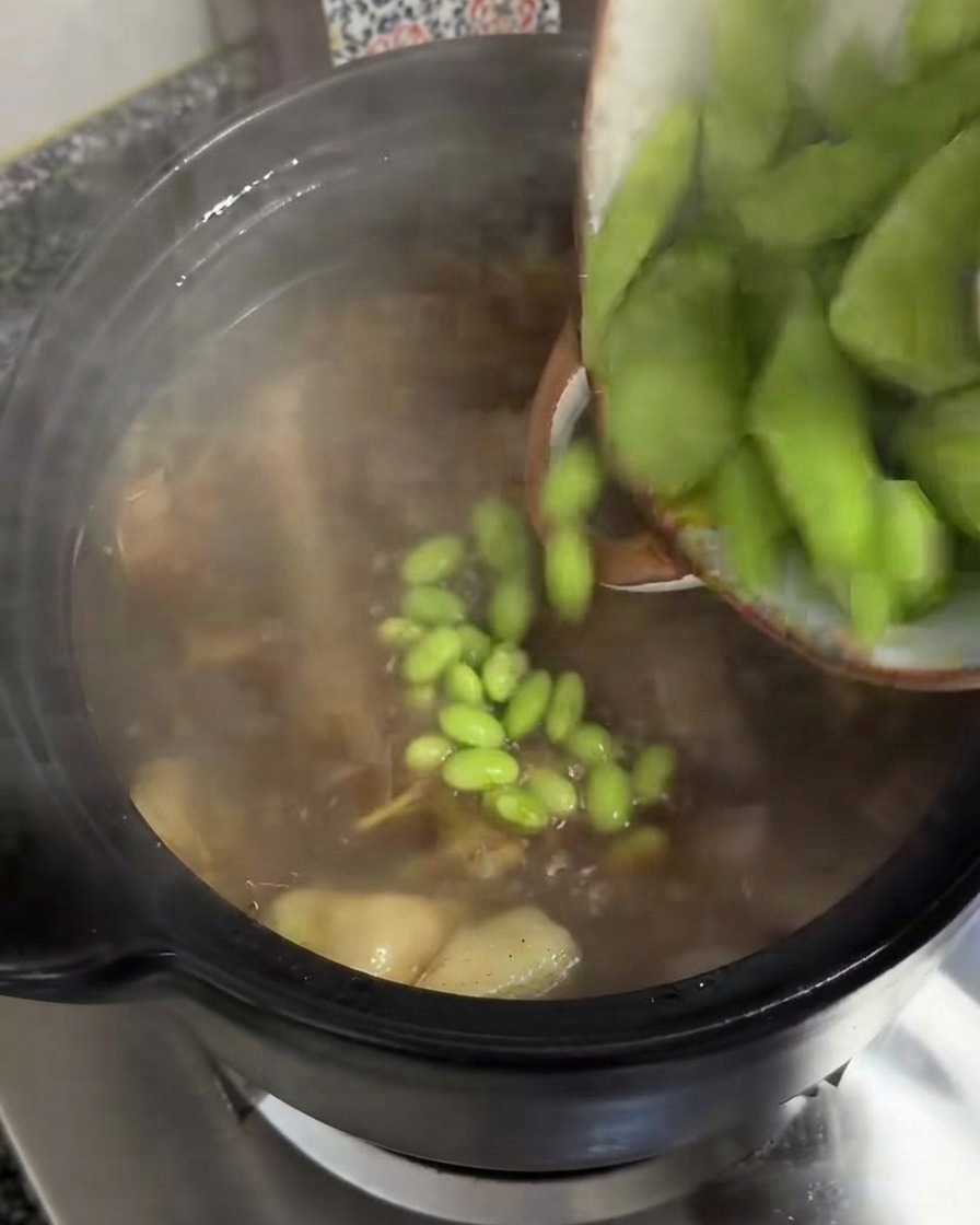 Rodajas gruesas de celtuce verde cayendo desde un bol a una olla de sopa humeante.
