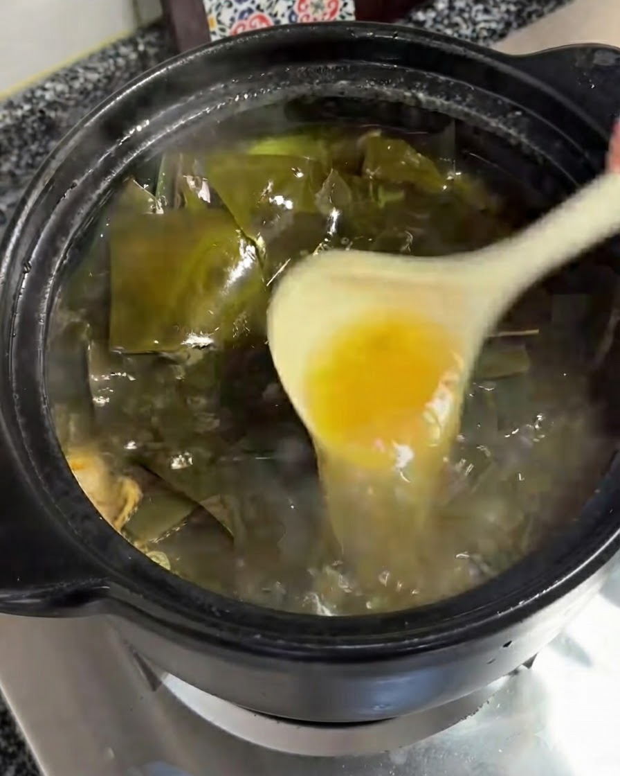 Un cucharón retirando una capa de aceite amarillento de la superficie burbujeante de la sopa.