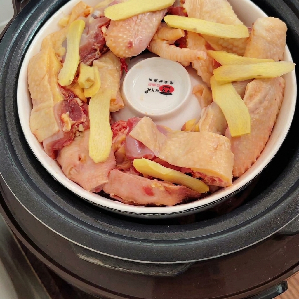 Rodajas de jengibre fresco dispuestas sobre los trozos de pollo dentro de la olla.