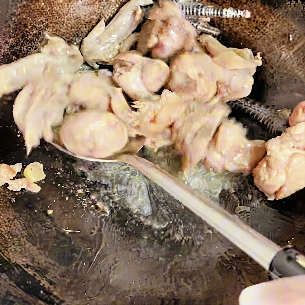 Trozos de pollo siendo removidos y salteados con una espátula en el wok hasta que estén ligeramente dorados.