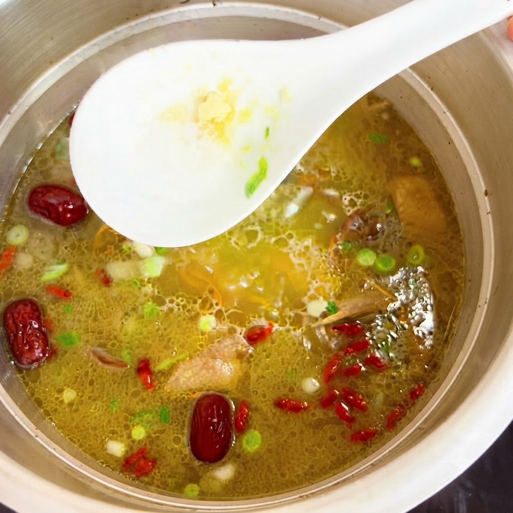 Esencia de pollo siendo removida en la olla de sopa caliente con una cuchara blanca.