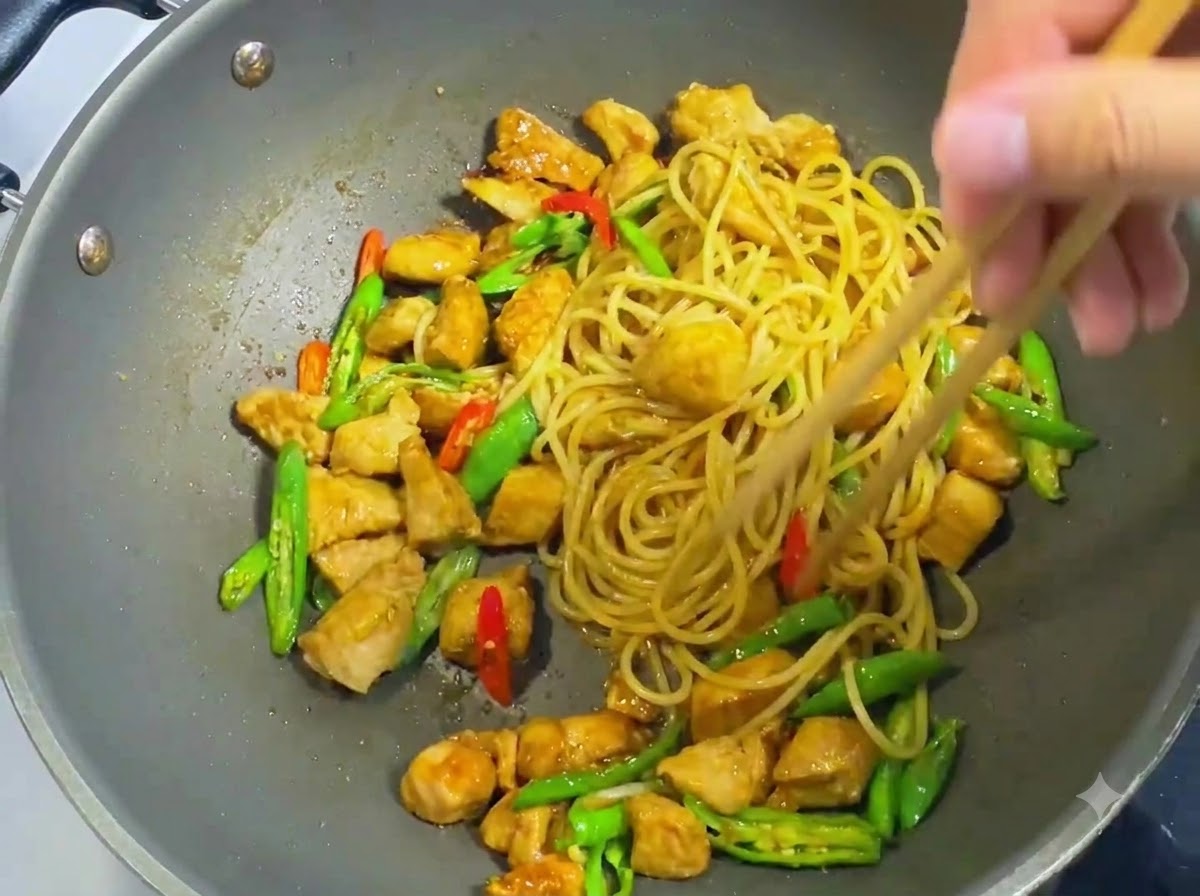 Palillos de madera mezclando espaguetis, pollo en cubos, chiles en rodajas y salsa oscura de manera uniforme en un wok.
