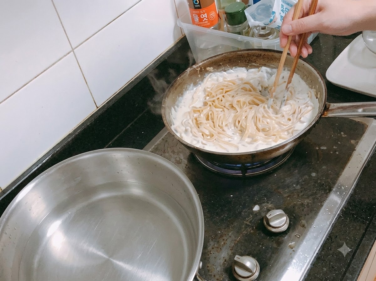 Pasta siendo mezclada en una salsa de crema a fuego lento en una sartén usando palillos.
