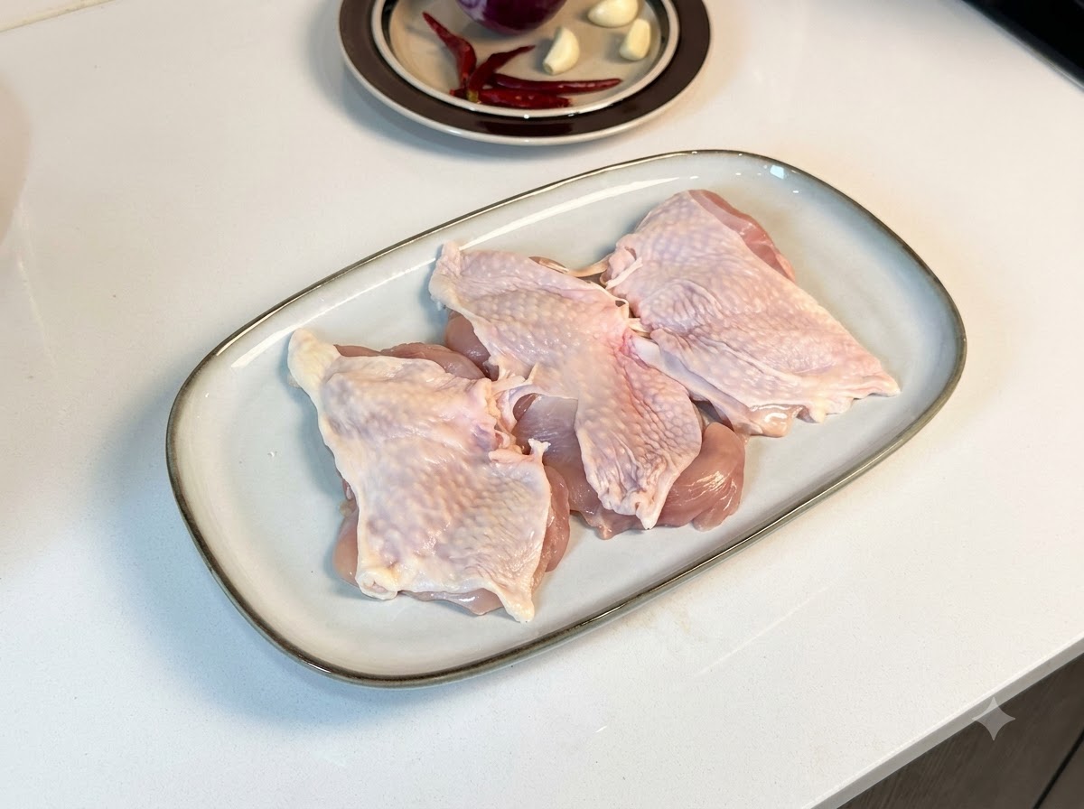Muslos de pollo deshuesados dispuestos en un plato blanco rectangular, cubiertos con pimienta negra y condimentos.