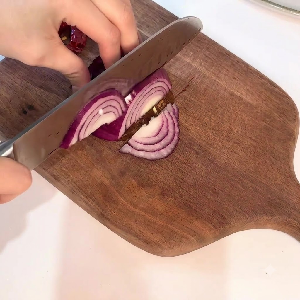 Una cebolla roja siendo rebanada cuidadosamente con un cuchillo en forma de media luna sobre una tabla de madera.